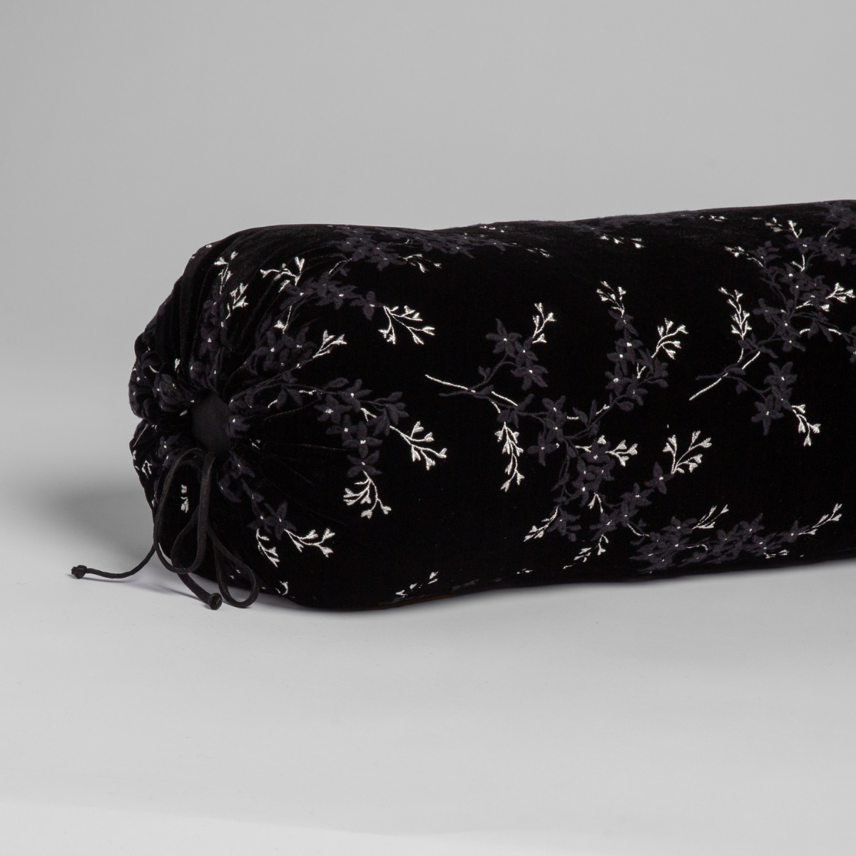 Close-up of Corvino velvet bolster pillow end with black cord ties and white floral embroidery.