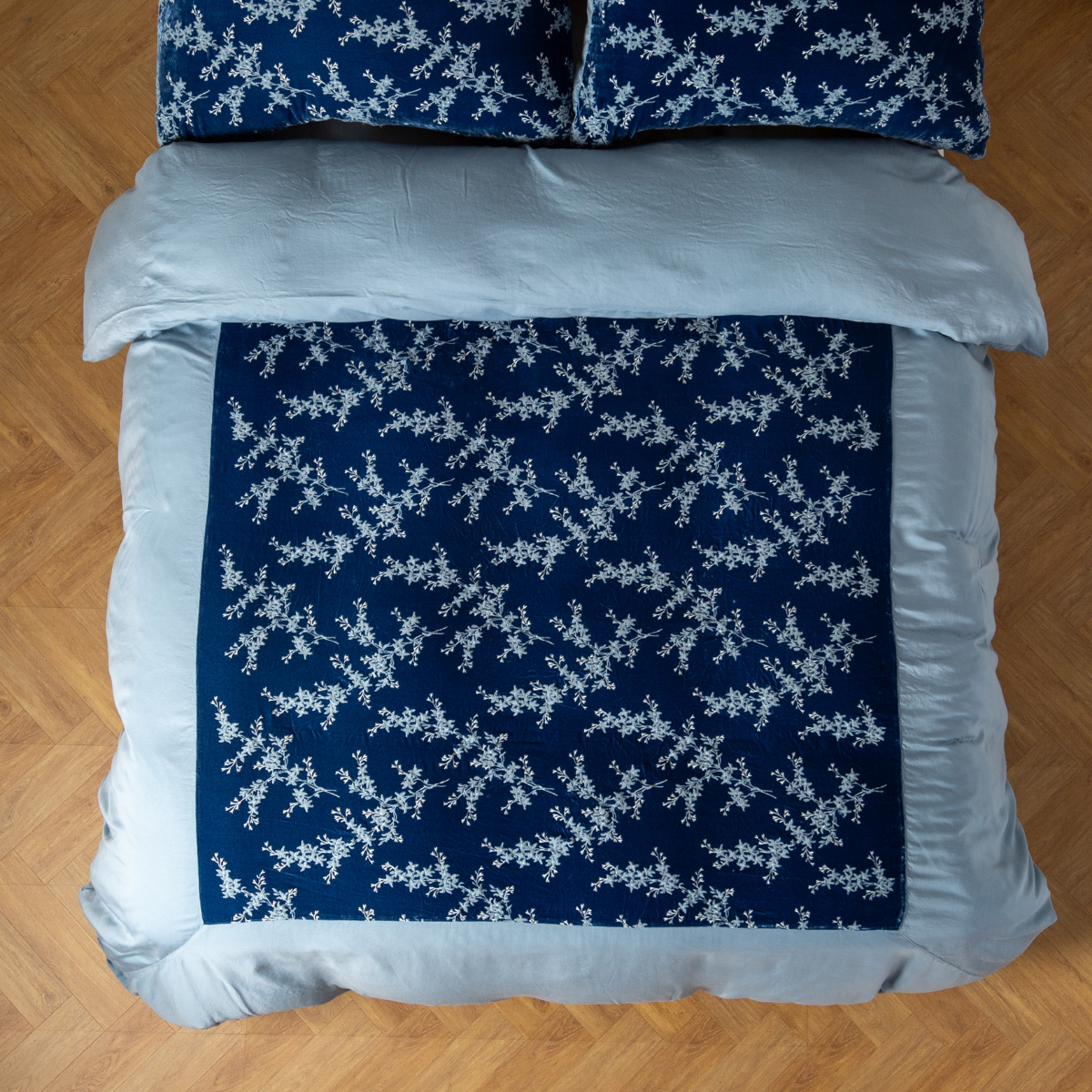 Overhead view of navy Tahoe Blue duvet with white floral vine print and pale blue border on wood floor.