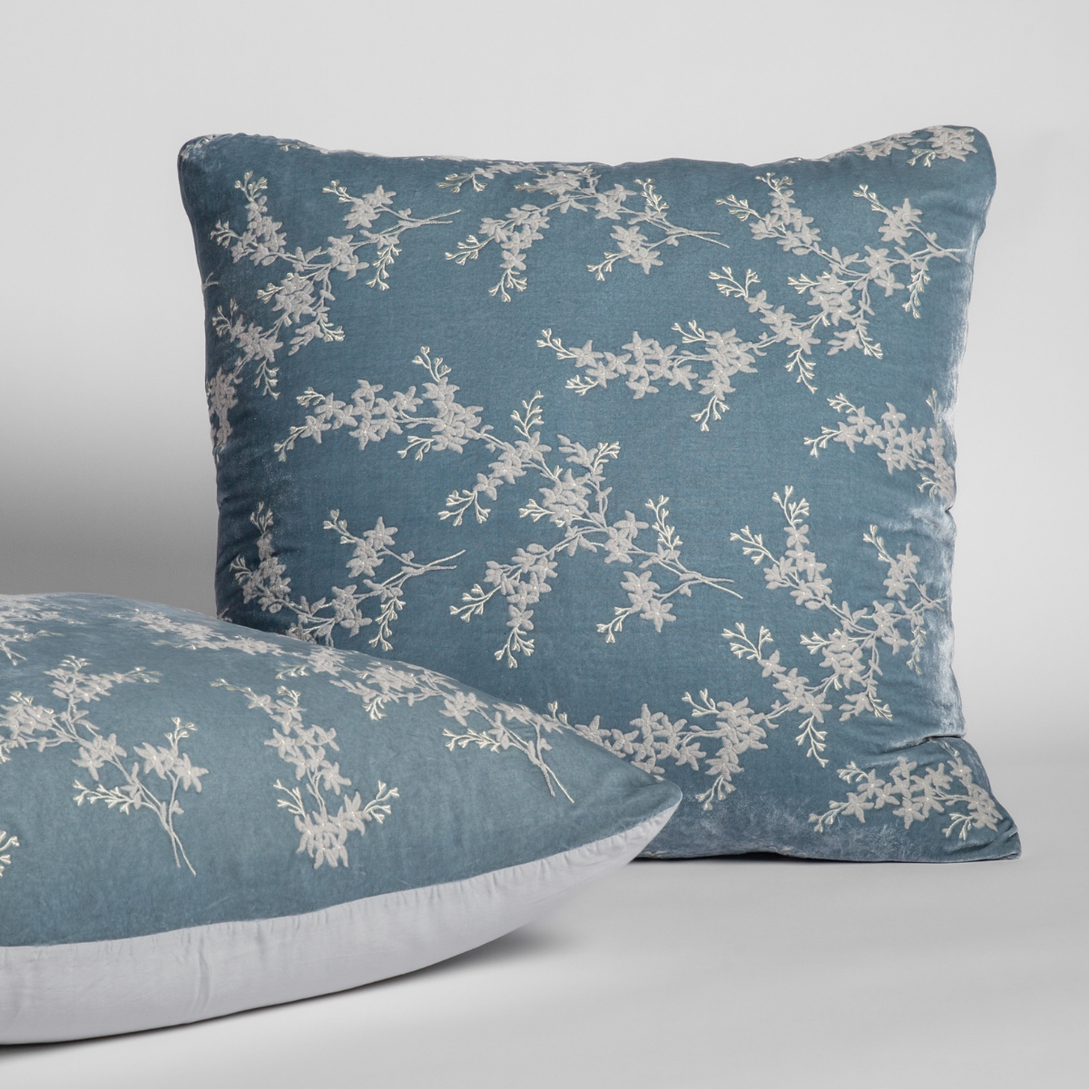 Lynette Luxe sham in Cloud, floral embroidery detail on two stacked pillows against neutral backdrop.