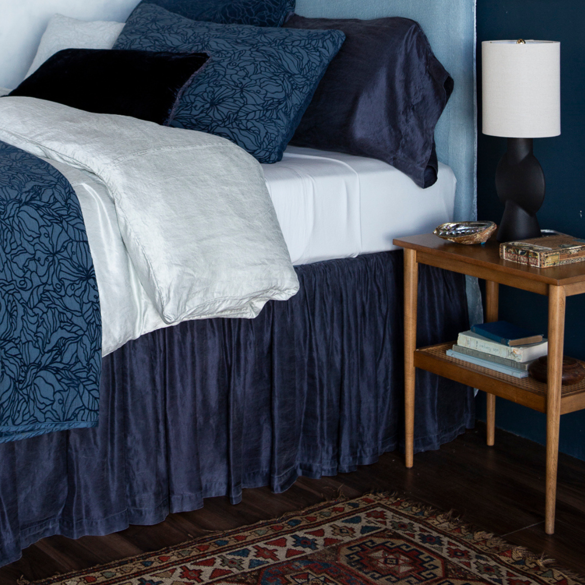 Midnight bed skirt with gathered ruffle styling, draped beside navy floral duvet in moody bedroom.