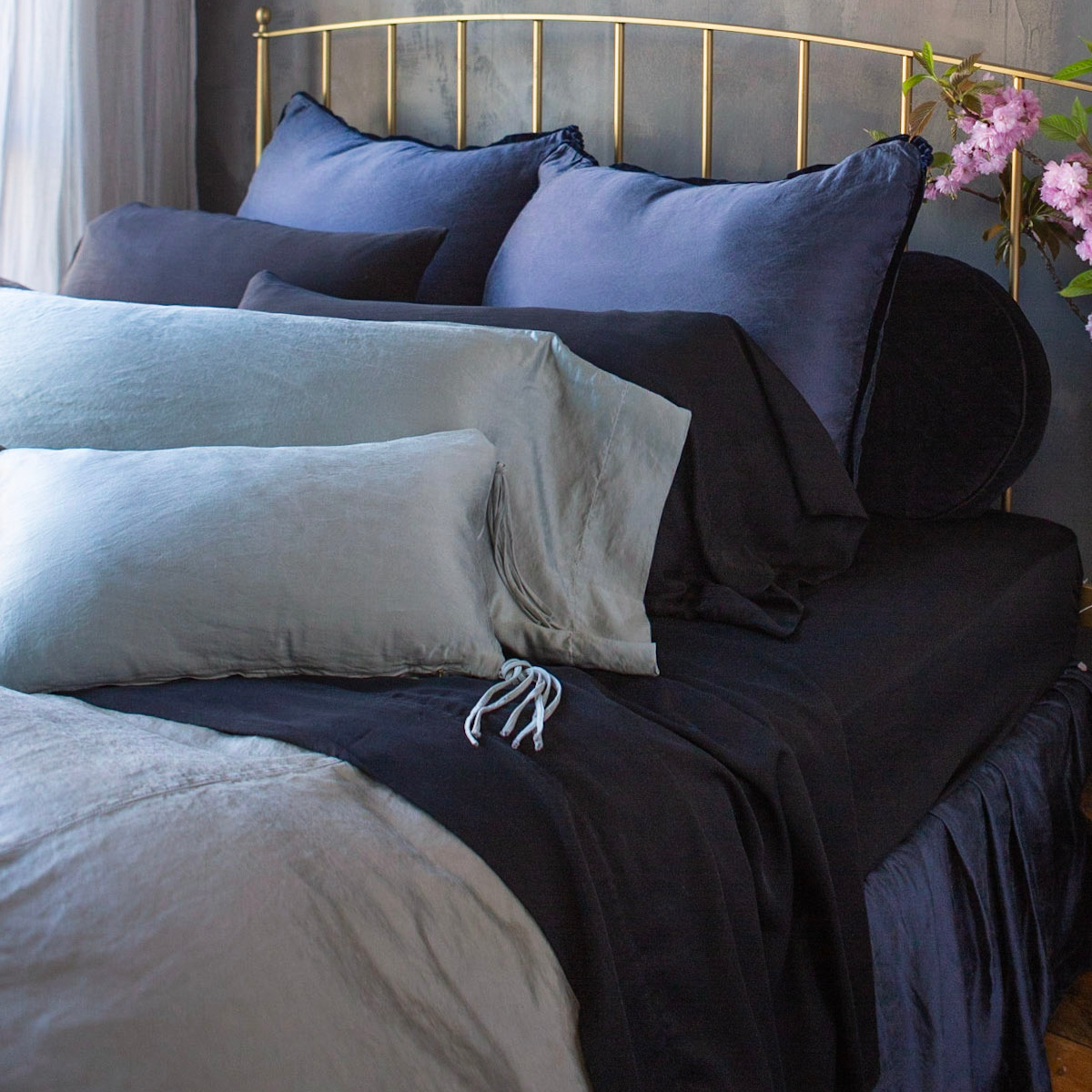 Midnight Paloma sham styled on bed with mixed navy and mist linen bedding, gold headboard.