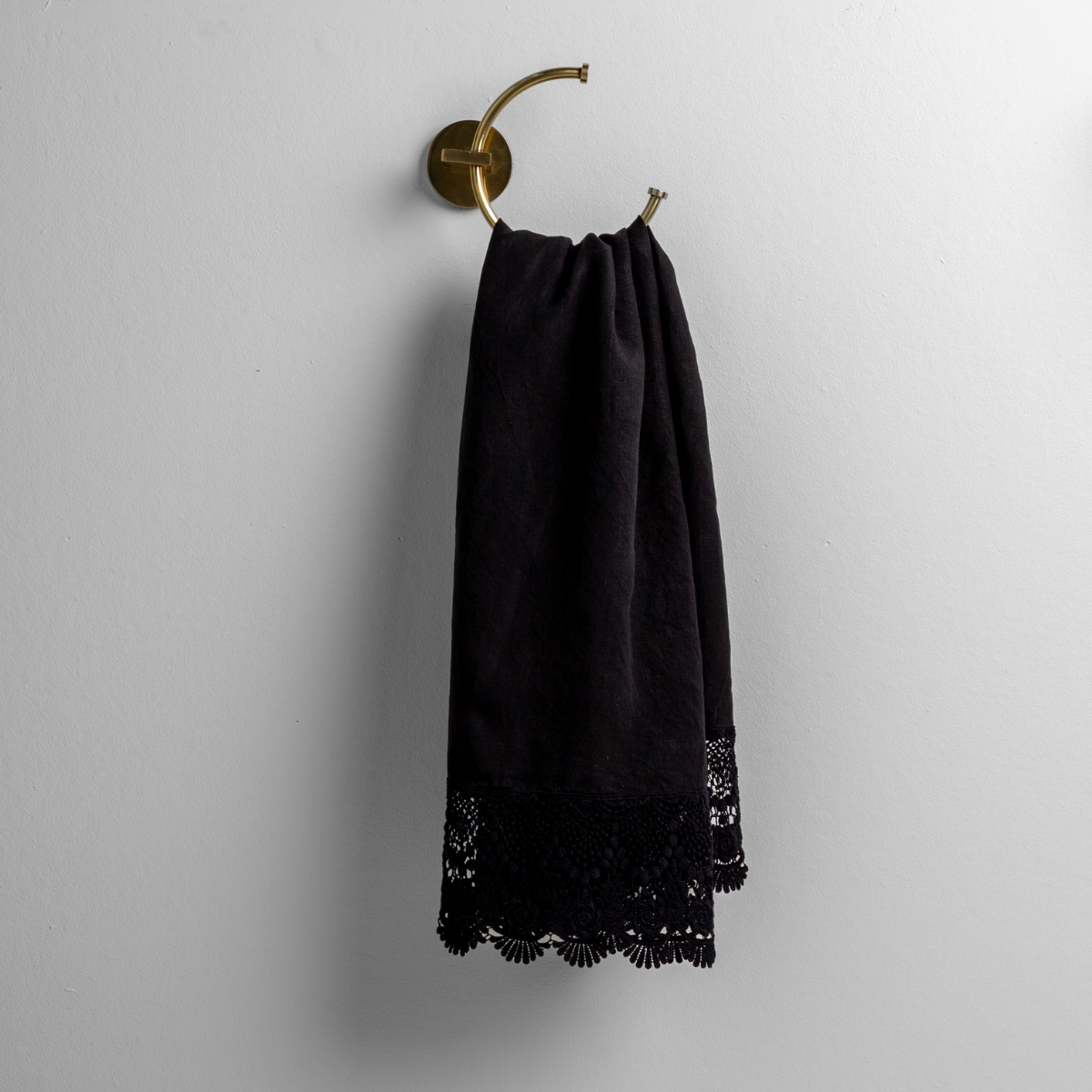 Corvino guest towel hung on brass ring hook, showing black lace trim detail at hem.