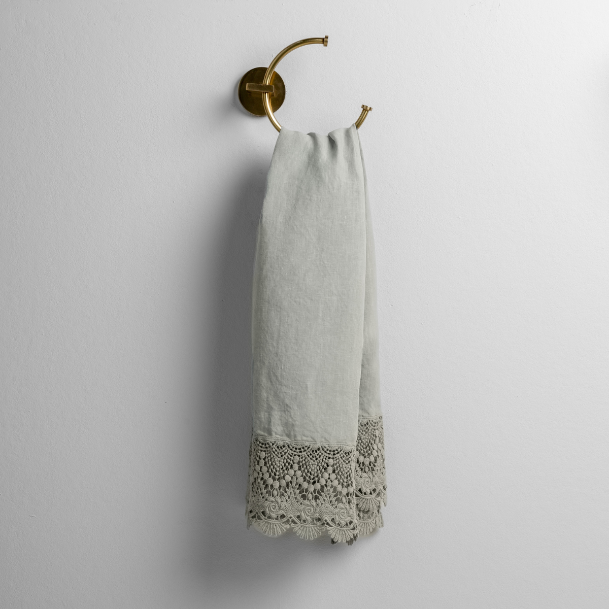 Mattine guest towel in Eucalyptus draped on brass ring, showing scalloped crochet lace trim detail.