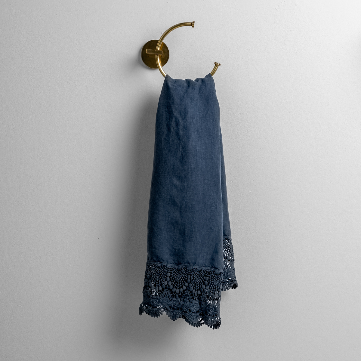 Midnight linen guest towel draped on brass ring, showing crochet lace trim detail at hem.