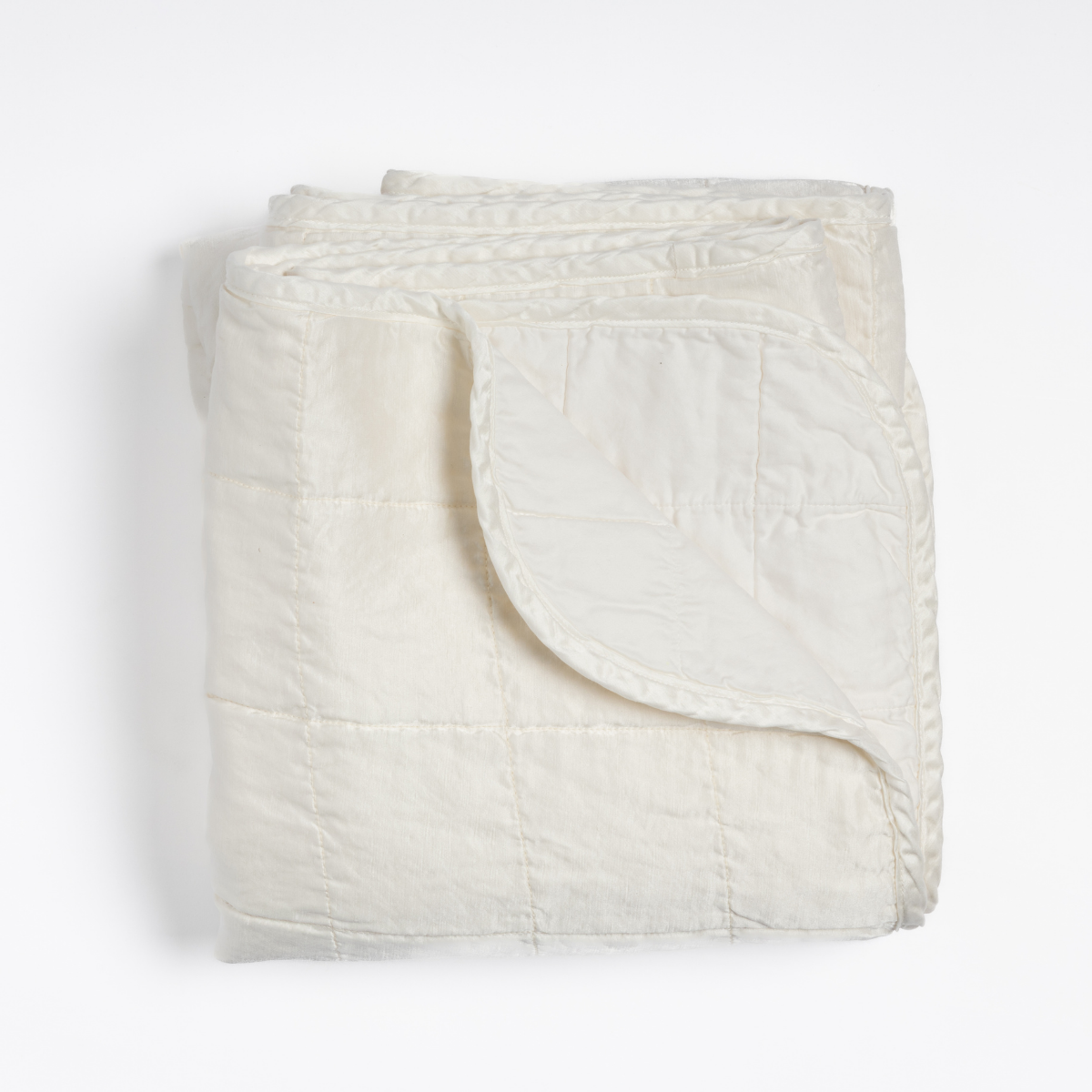 Sel blanket in Winter White, folded to show quilted stitching and softly curled corner.