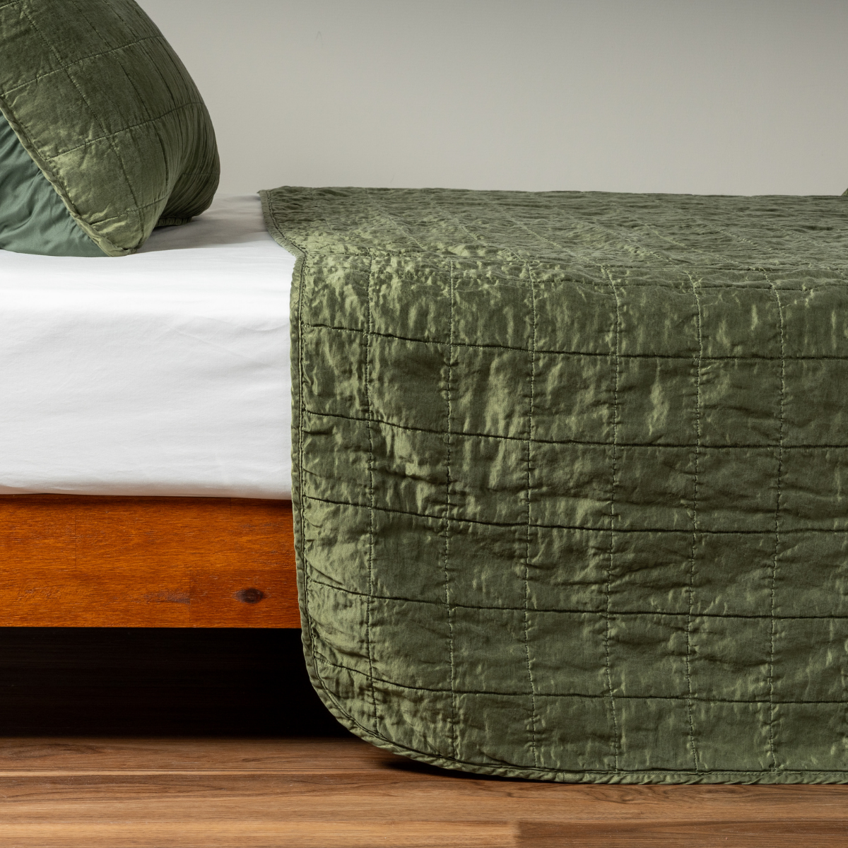 Juniper coverlet draped over foot of wooden bed, showing quilted texture and relaxed linen drape.