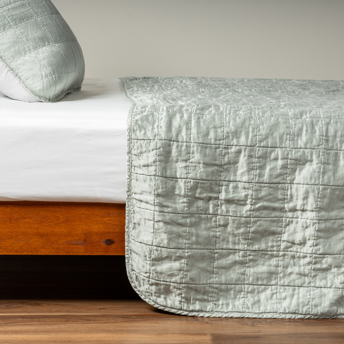 Eucalyptus coverlet draped over bed foot, showing quilted grid stitching and crinkled texture.
