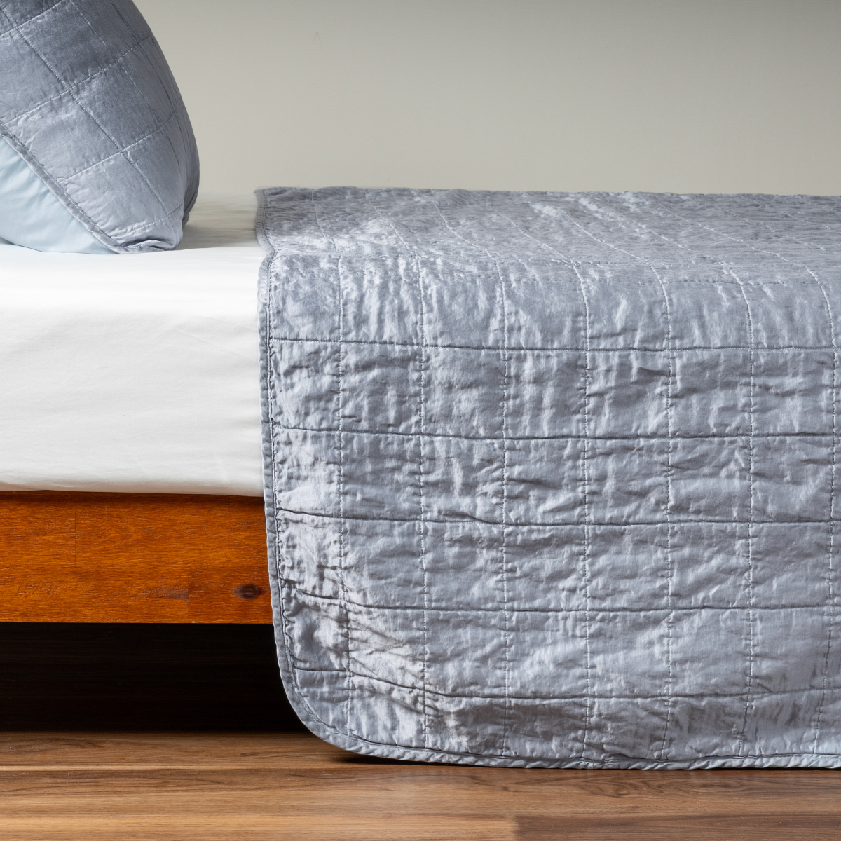 Tahoe Blue coverlet draped over bed foot, showing quilted square stitching and lustrous sheen.