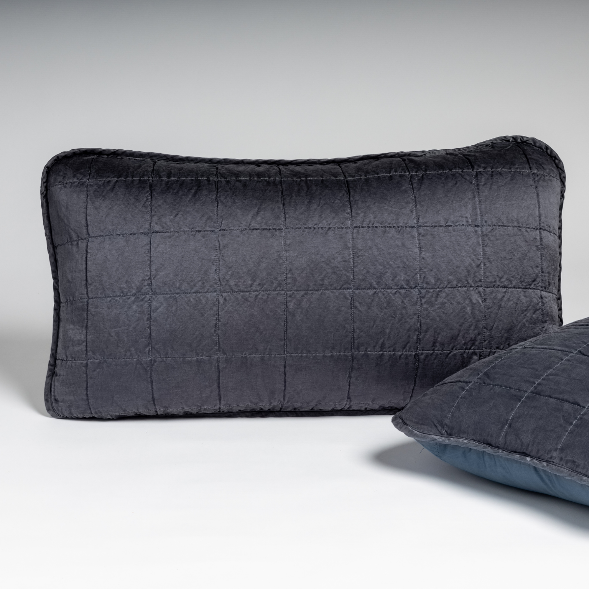 Midnight quilted lumbar sham with grid stitching, second sham partially visible at right.