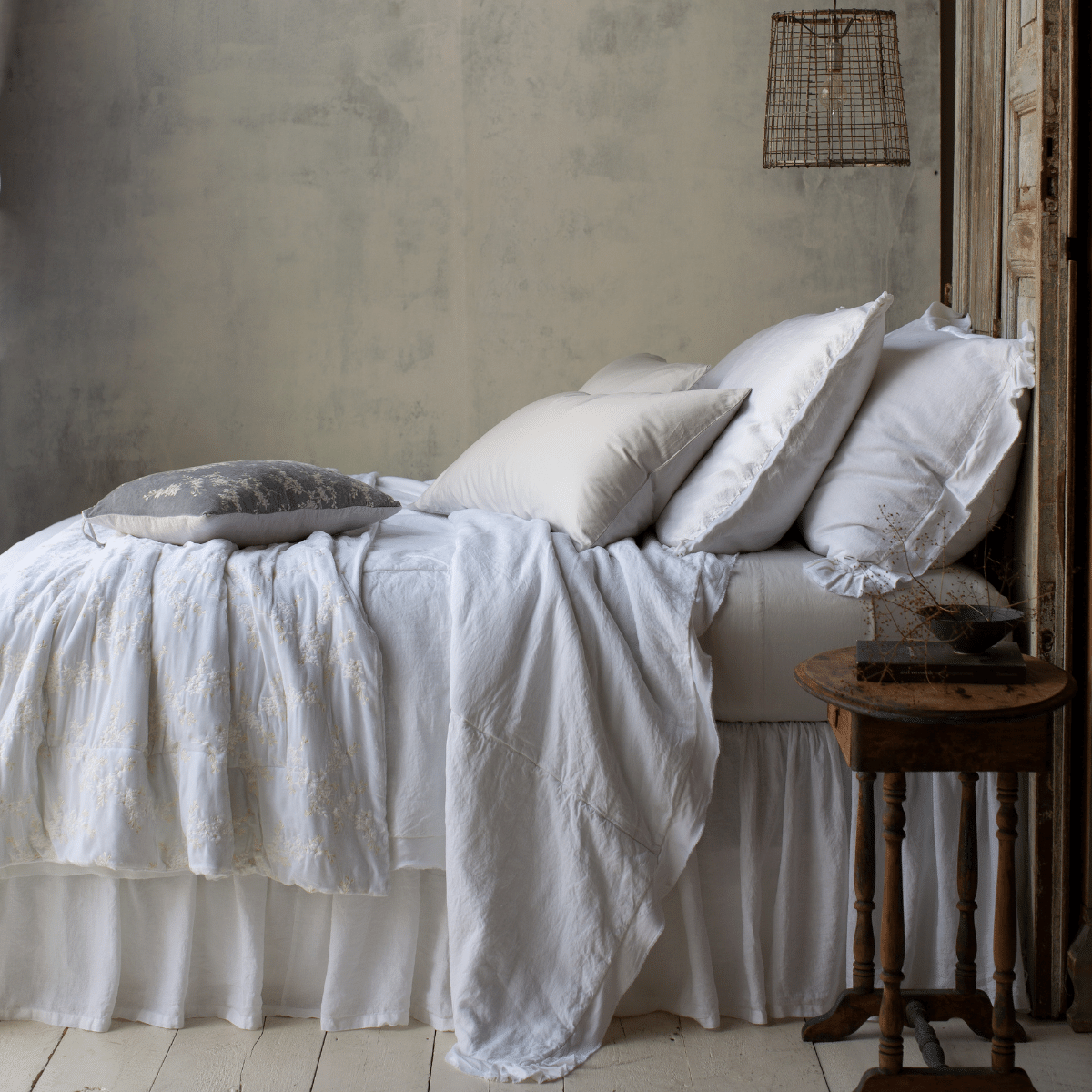 Bella Notte Lynette blanket in White, draped over a bed in a rustic styled bedroom.