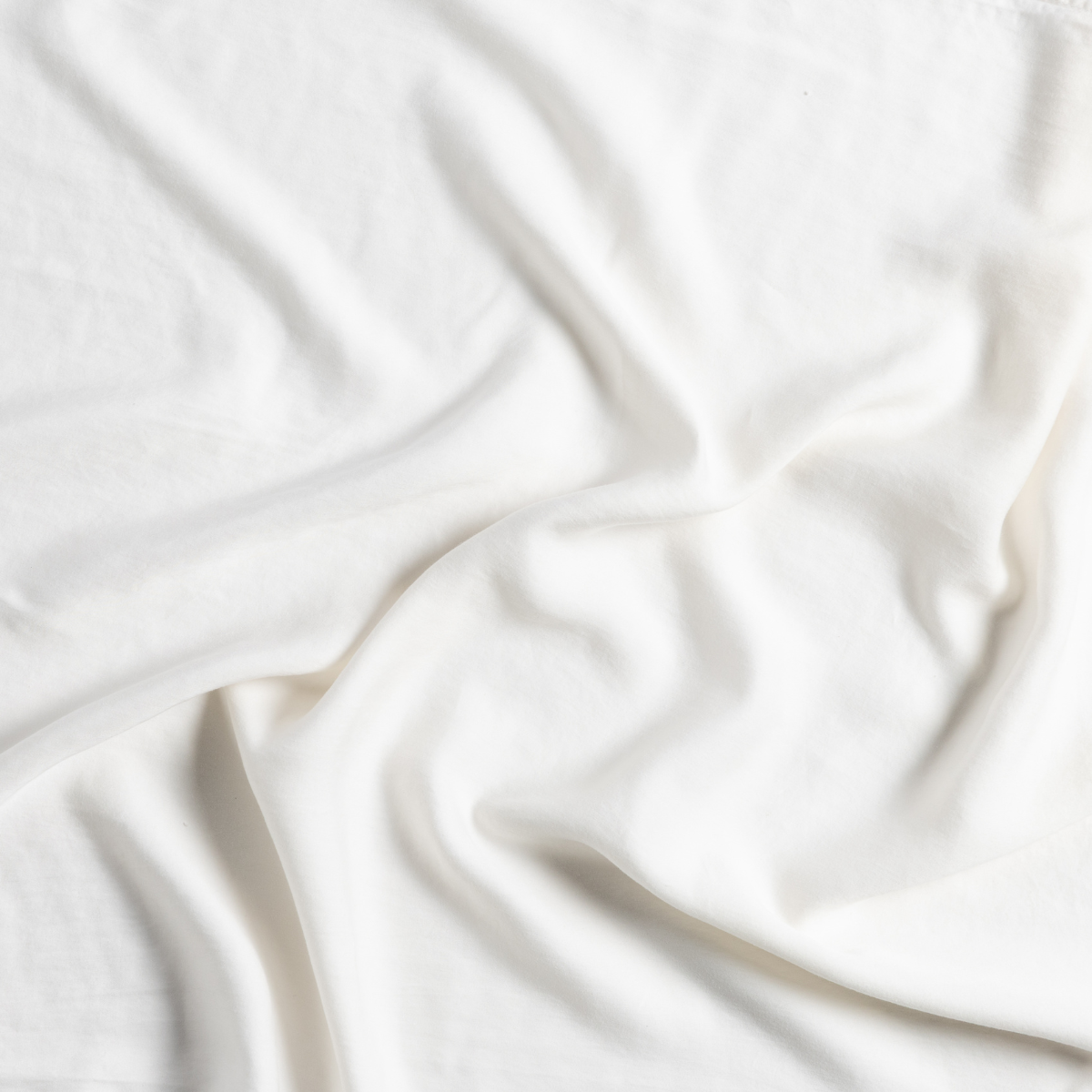 Close-up of draped Natural Madera Luxe flat sheet showing silky fabric folds and soft sheen.