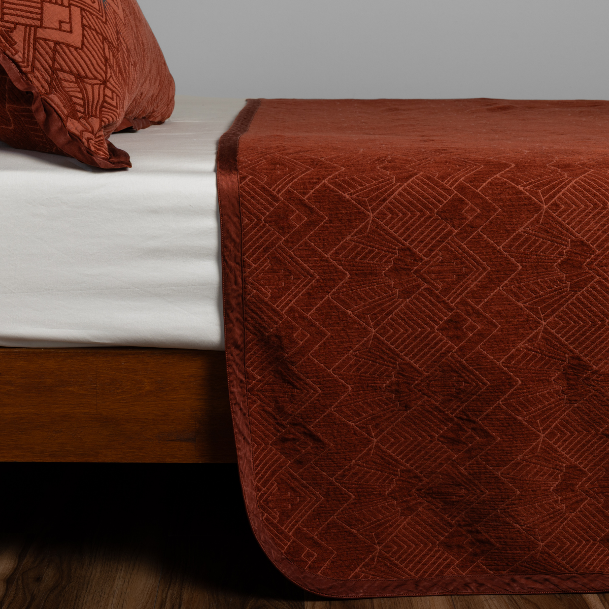 Autumn Trettino bedspread draped over bed foot, showing geometric jacquard pattern detail.