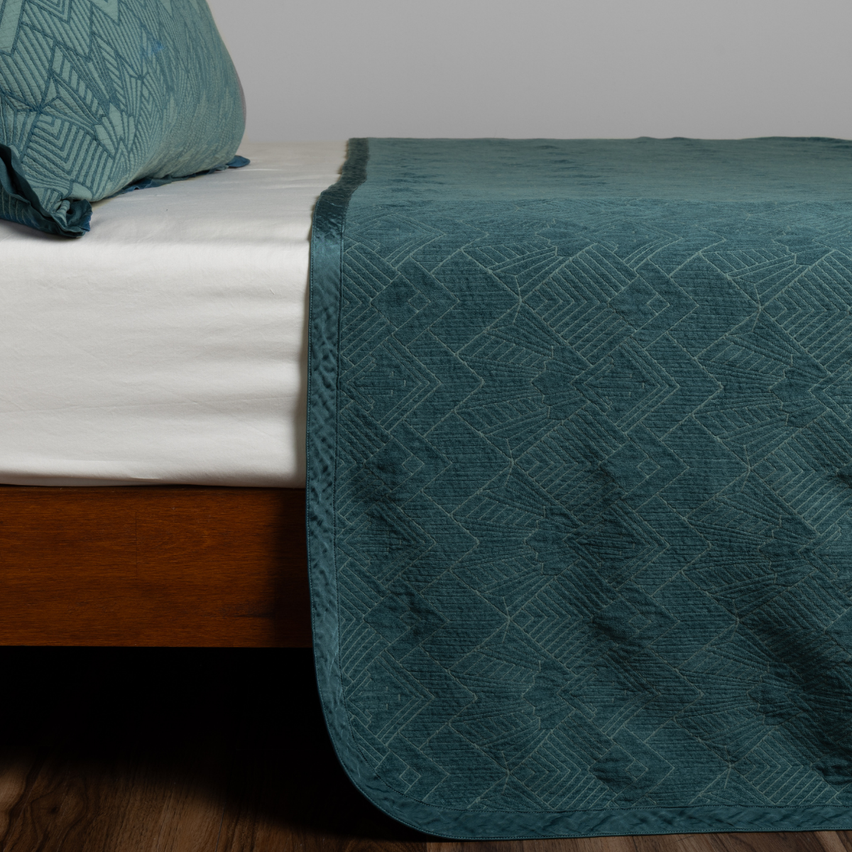 Cenote bedspread draped over bed foot, showing geometric diamond jacquard texture.