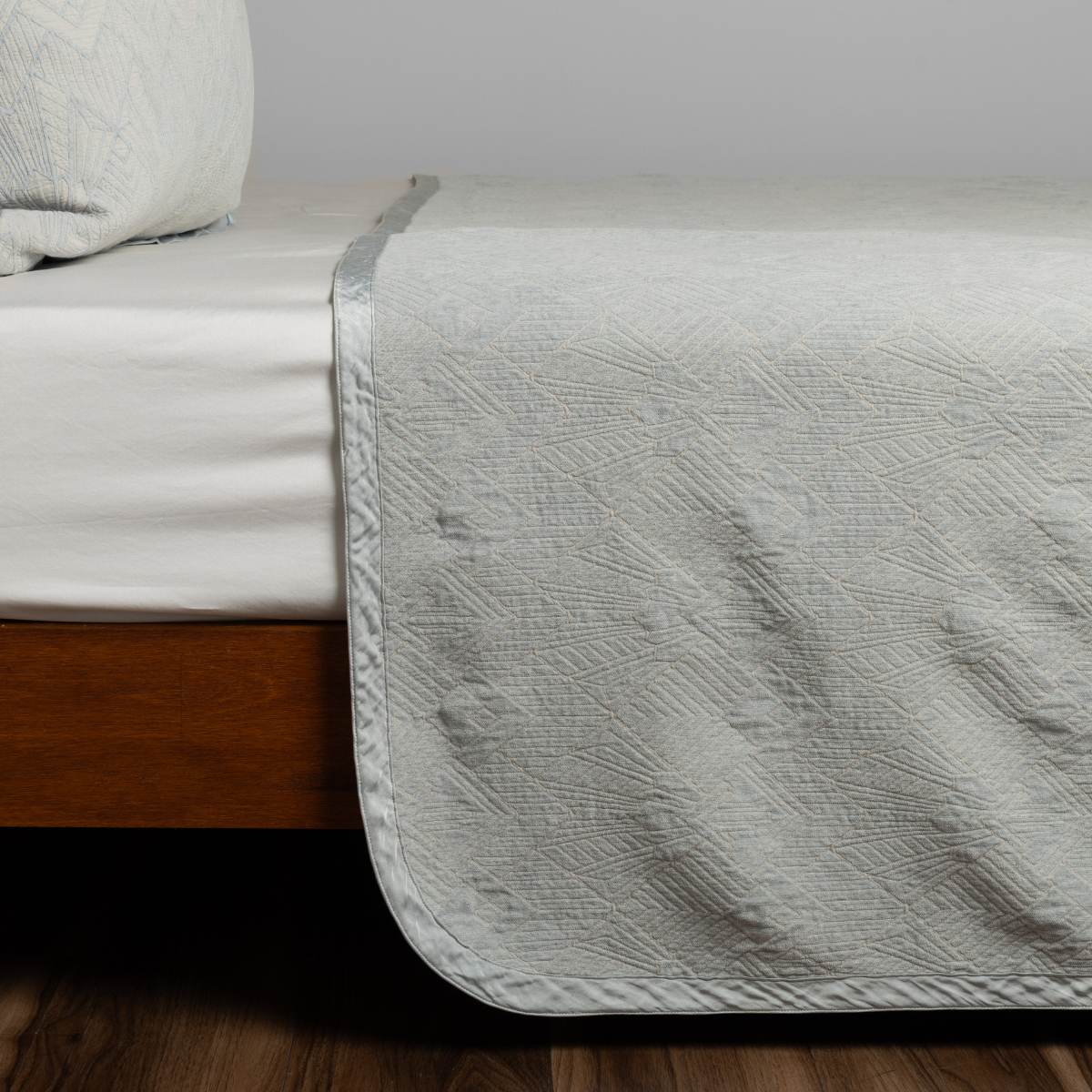 Foot-of-bed view of Cloud Bella Notte Trettino bedspread draping over wooden bed frame.