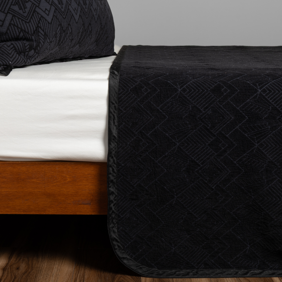Bella Notte Trettino bedspread in Corvino draped over bed foot, showing tonal geometric quilted texture.