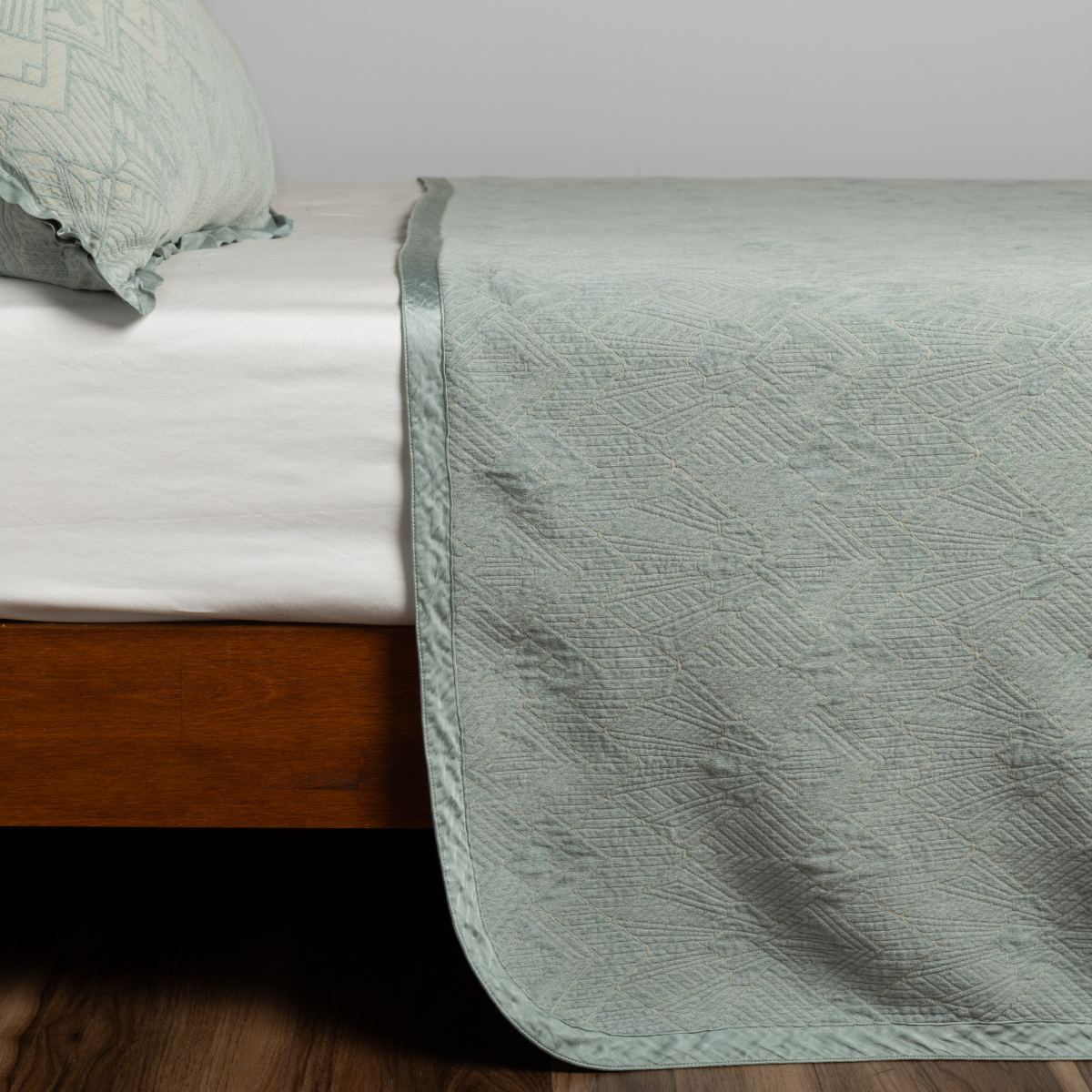 Eucalyptus bedspread draped over bed foot, showing quilted geometric texture and satin border trim.