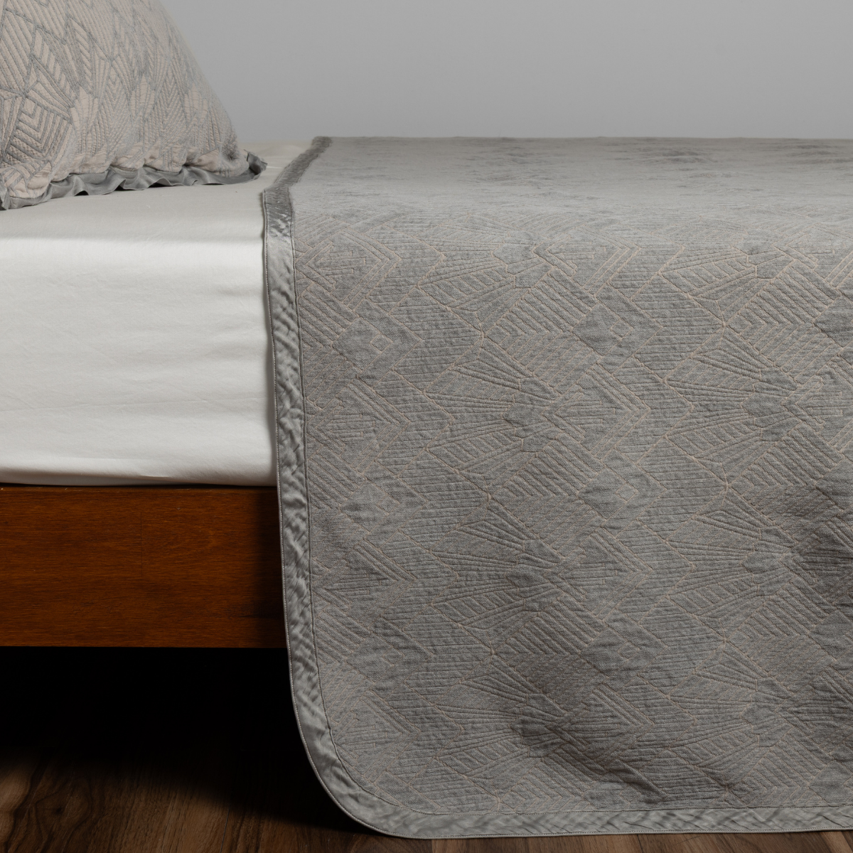 Close-up of Fog Bella Notte Trettino bedspread draped over bed foot, showing quilted diamond texture.