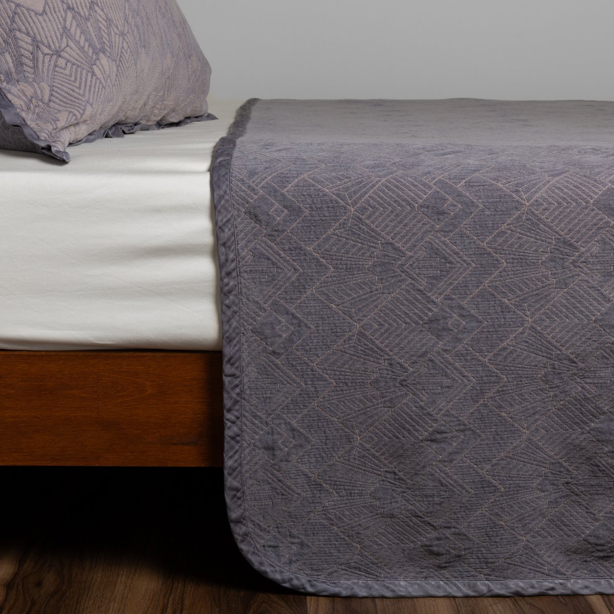 Foot-of-bed view showing French Lavender Trettino bedspread's geometric jacquard texture.