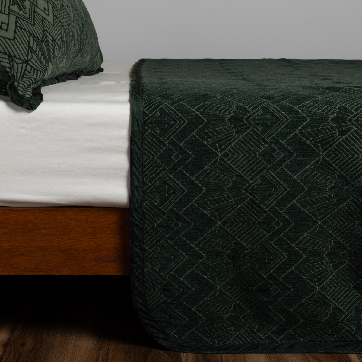 Juniper Trettino bedspread draped over bed foot, geometric jacquard pattern in deep green tones.