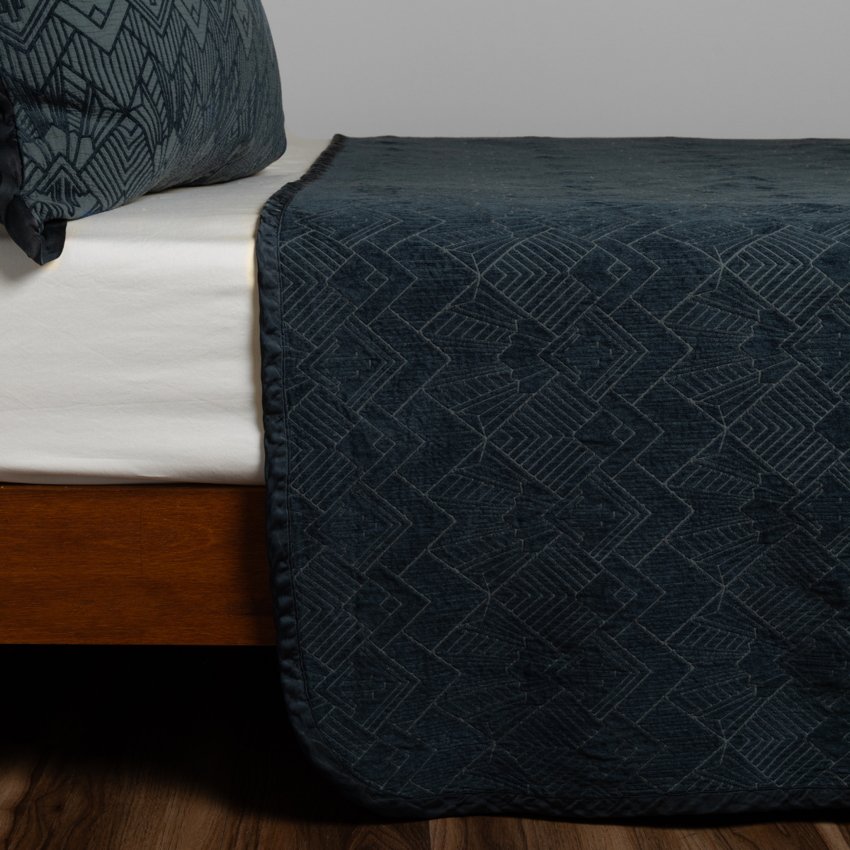 Midnight Trettino bedspread draped over bed foot, showing geometric quilted pattern detail.