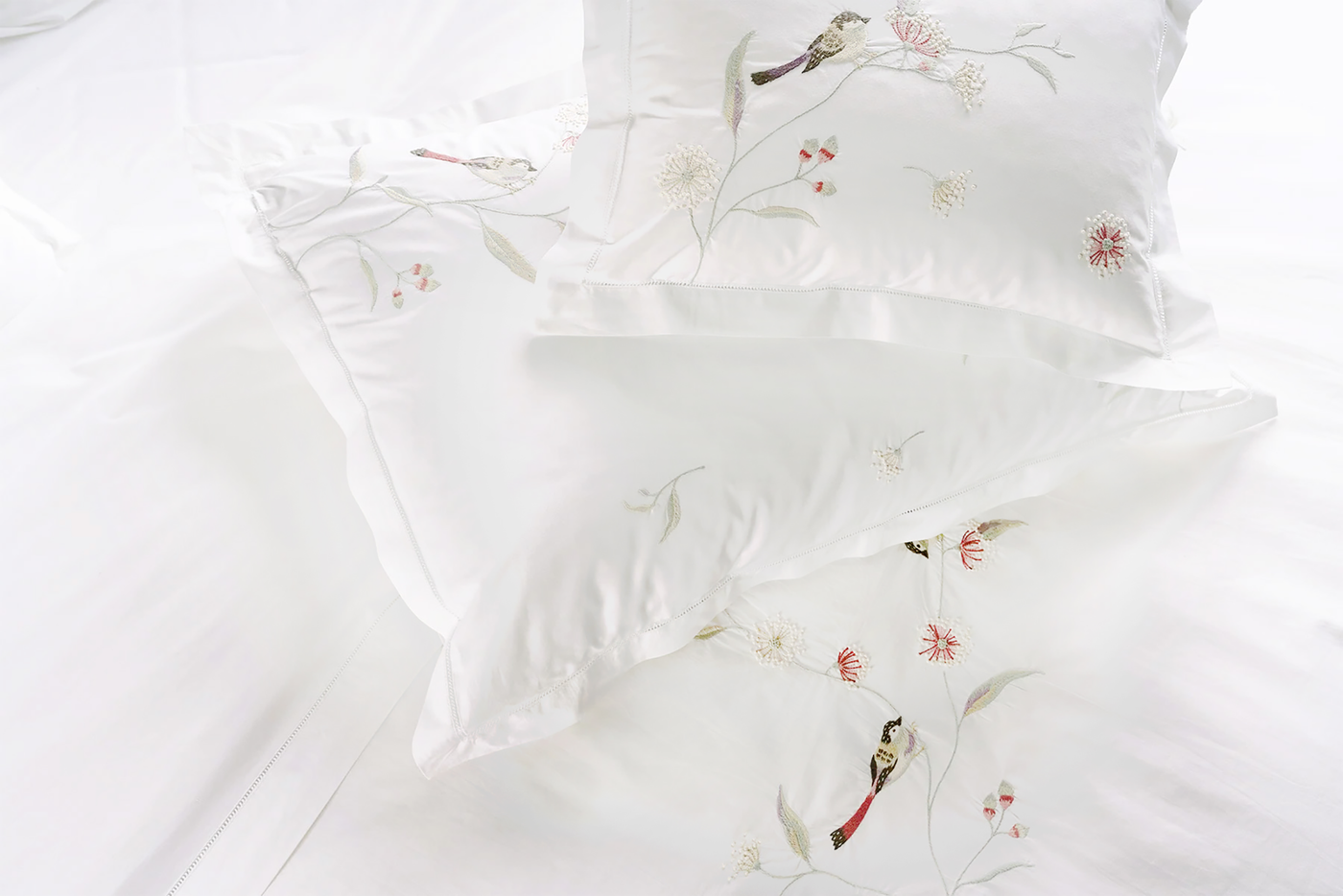 Overhead view of white pillowcases with embroidered birds and floral branches.