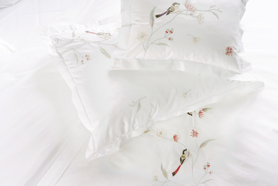 Overhead view of white pillowcases with embroidered birds and floral branches.