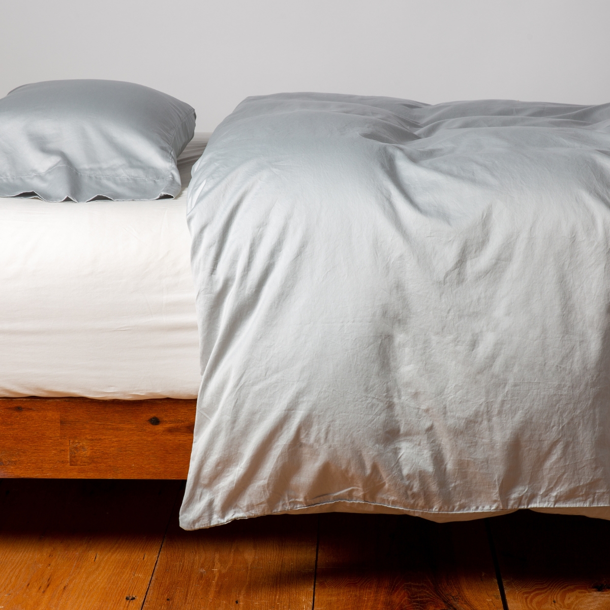 Bella Notte Bria duvet cover in Cloud, draped over a low wood-frame bed with matching pillowcase.
