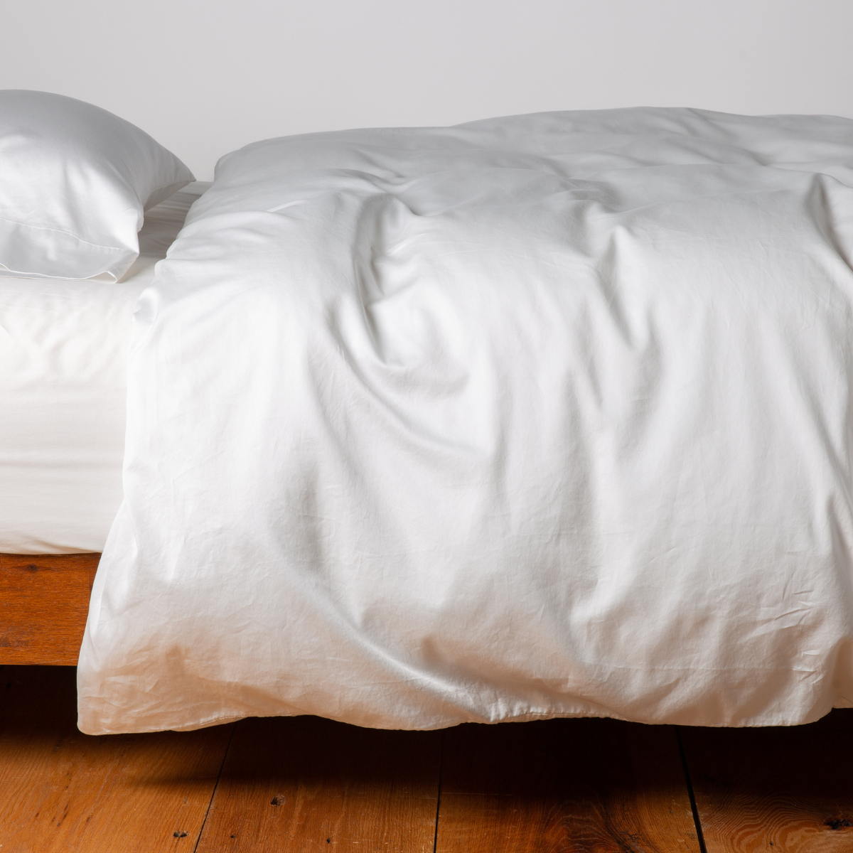 Bella Notte Bria duvet cover in Winter White, softly rumpled on a low wood bed.