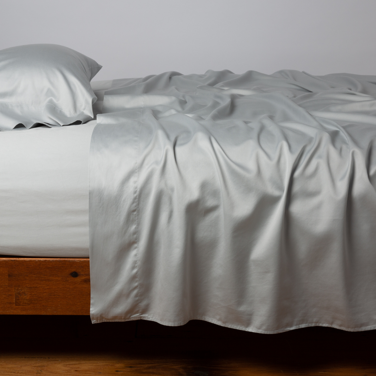Bria fitted sheet in Cloud draped loosely over a wood-framed bed with matching pillowcase.