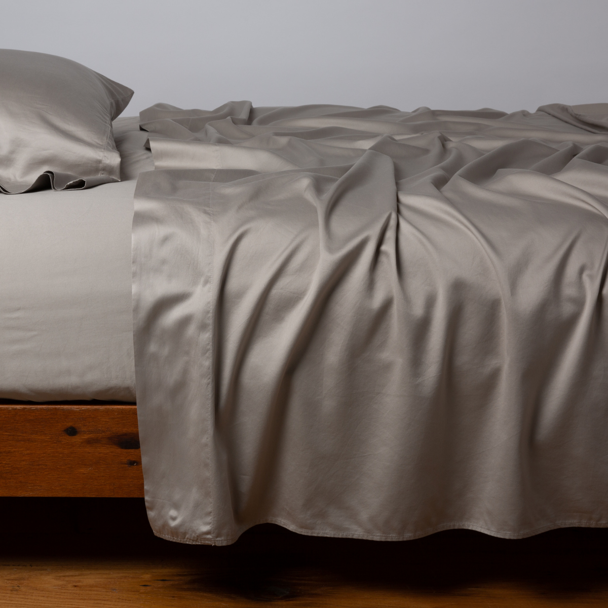 Fog fitted sheet draped loosely over a wood-frame bed, showing lustrous sateen sheen.