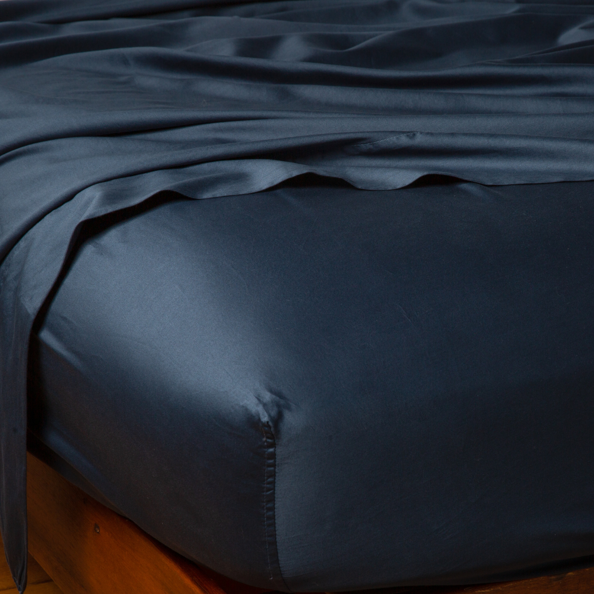 Corner detail of Bella Notte Bria fitted sheet in Midnight, showing silky drape on bed.