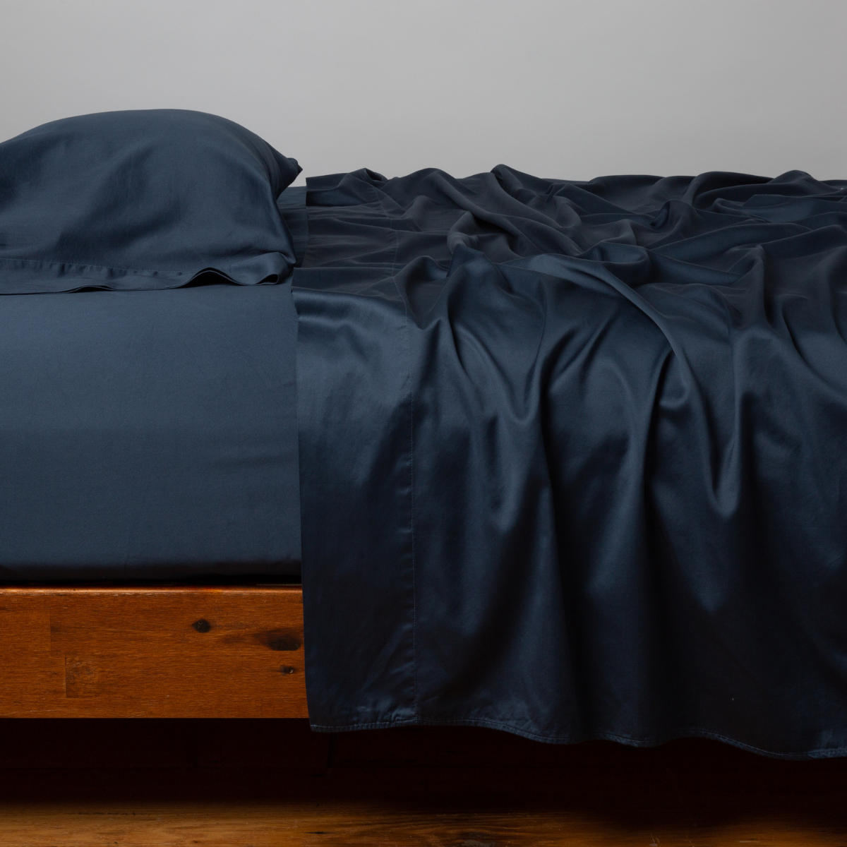Midnight fitted sheet draped over wood bed frame, lustrous sateen finish.