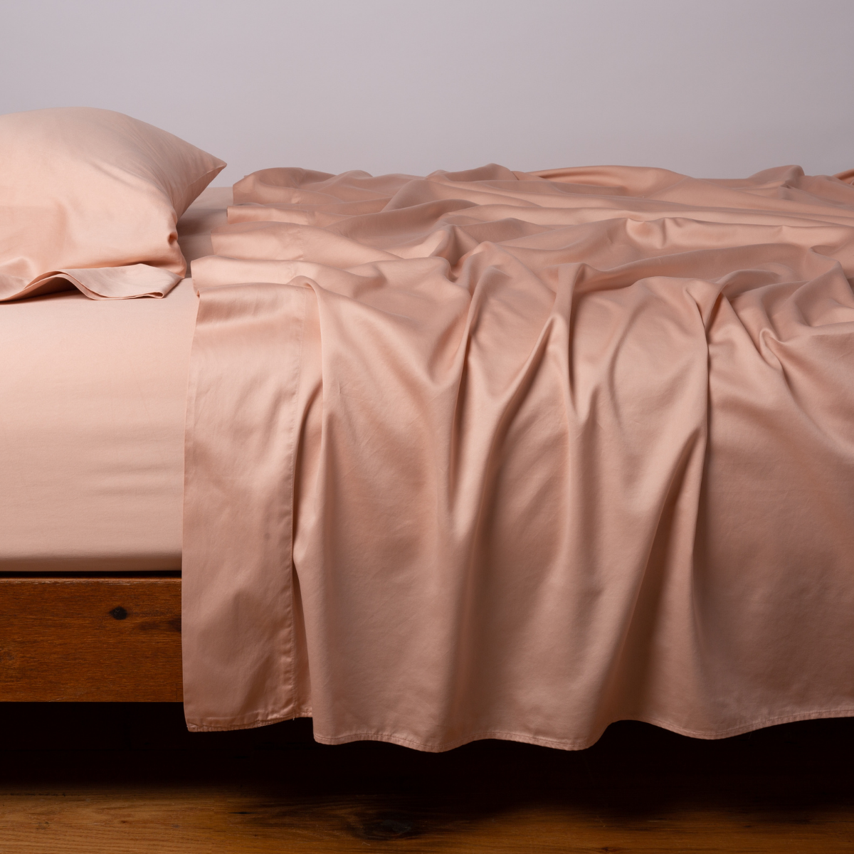 Blushed sateen fitted sheet draped loosely over a wood-frame bed with matching pillowcases.