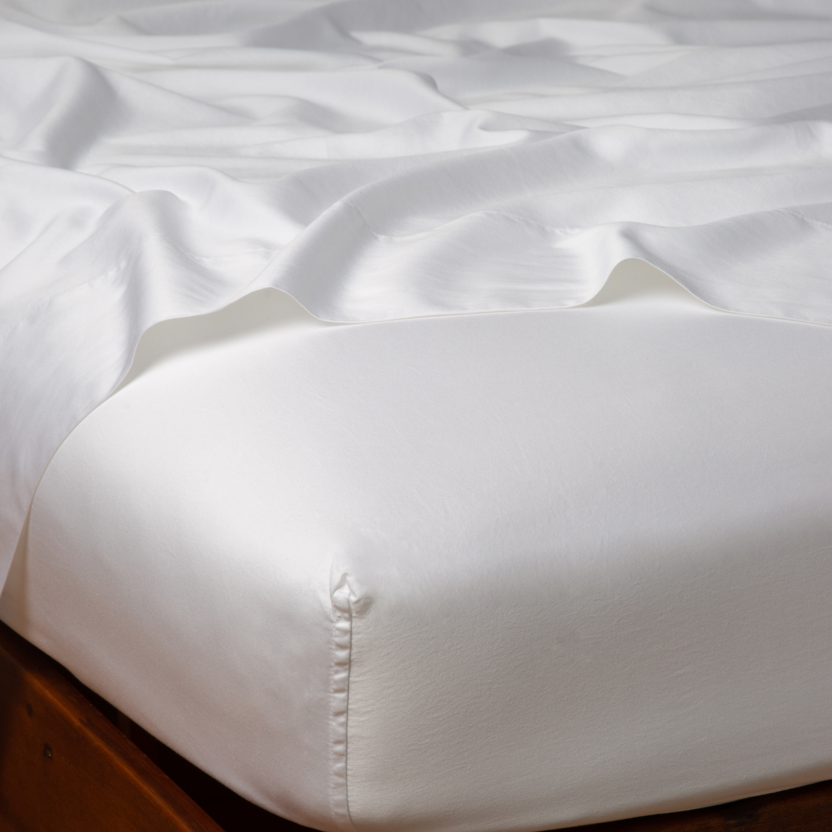 Bella Notte Bria fitted sheet in White, smooth fabric on bed with natural wood frame.