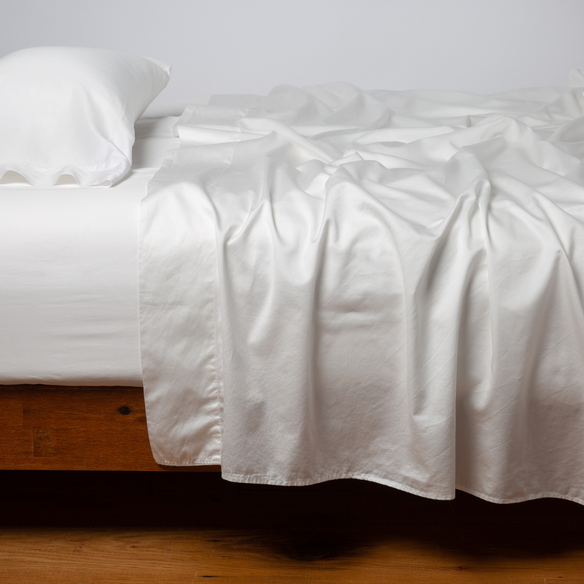 Winter White fitted sheet draped loosely over a wood-frame bed with matching pillowcase.