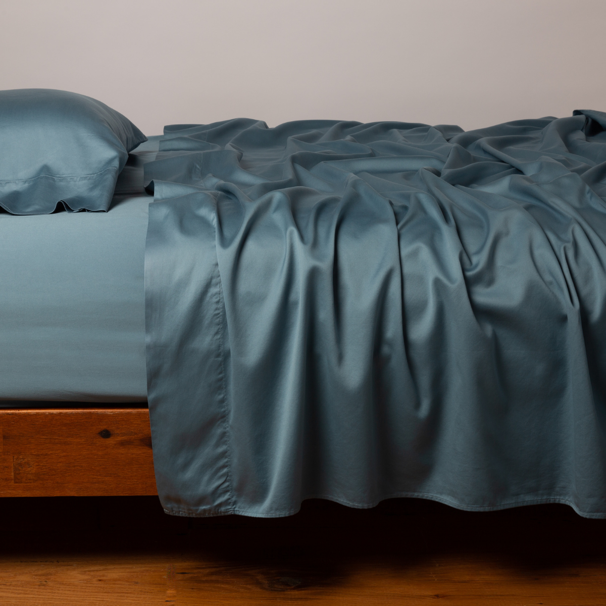 Bria flat sheet in Cenote draped loosely over a wood-frame bed with matching pillowcases.