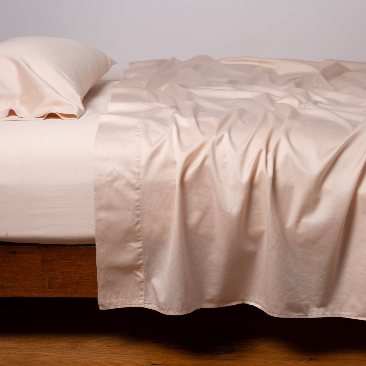 Bria flat sheet in Pearl draped loosely across a wood-framed bed with matching pillowcase.