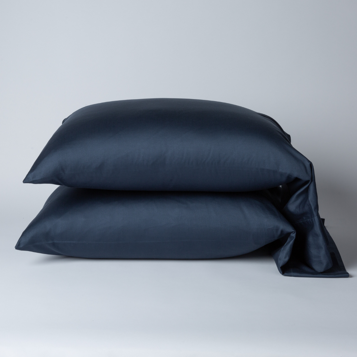 Two Midnight Bella Notte Bria pillowcases stacked, smooth sateen cotton, deep navy, one corner draped open.
