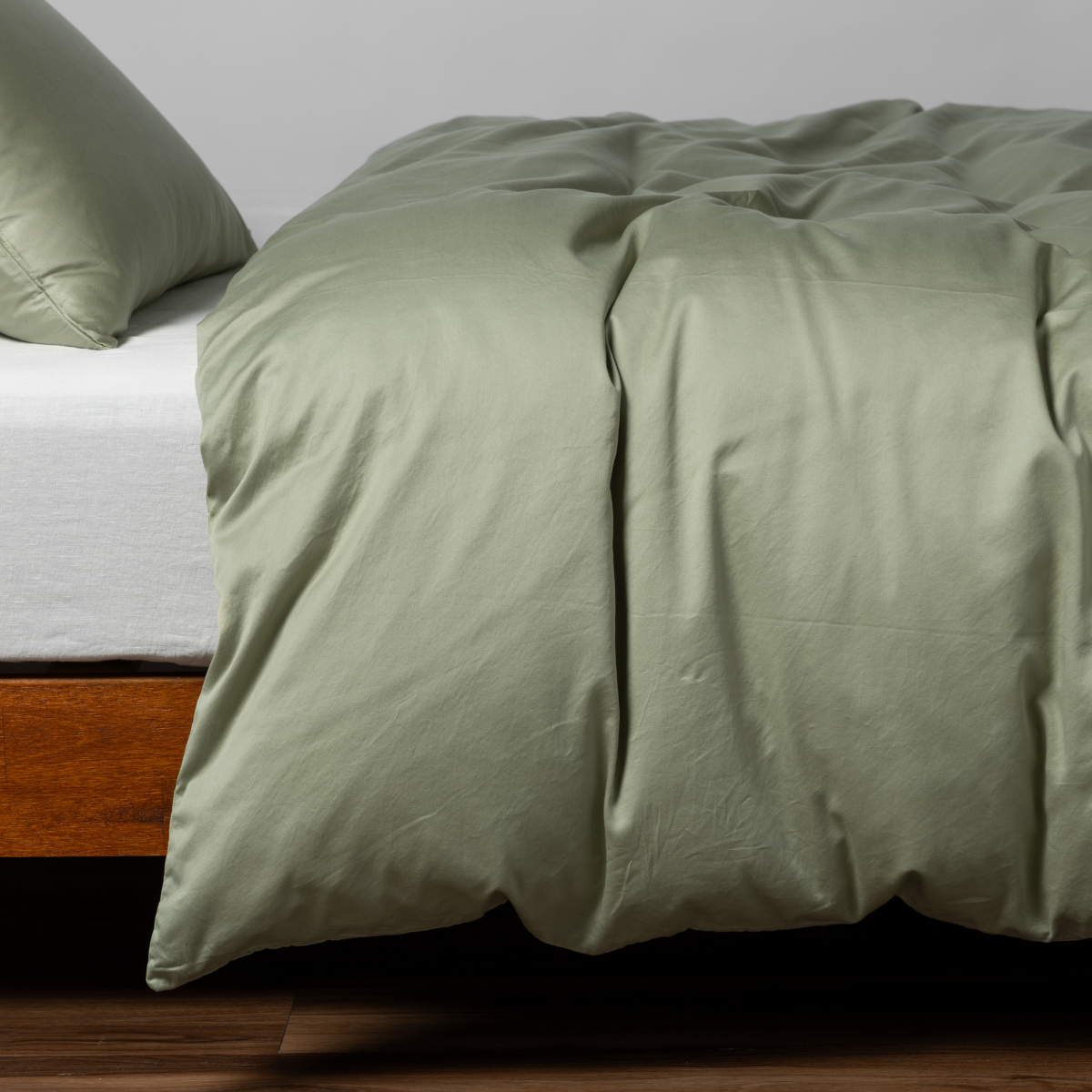 Bella Notte Bria duvet cover in Desert Sage draped over bed, silky smooth fabric with soft folds.