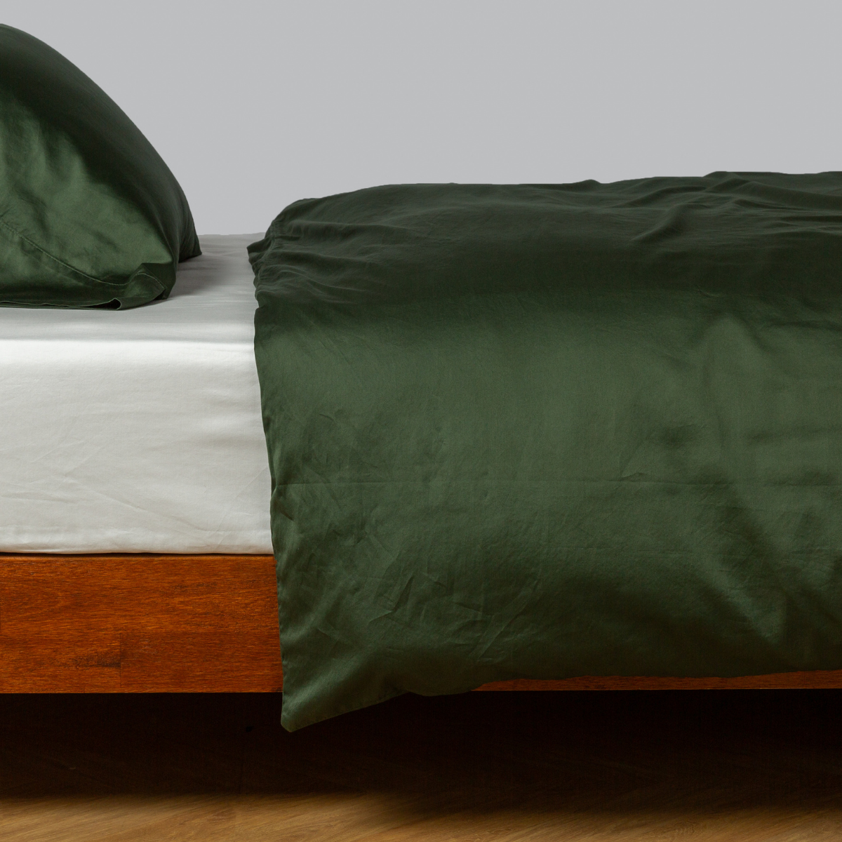 Bella Notte Bria duvet cover in Juniper draped over a wood-framed bed, side angle view.