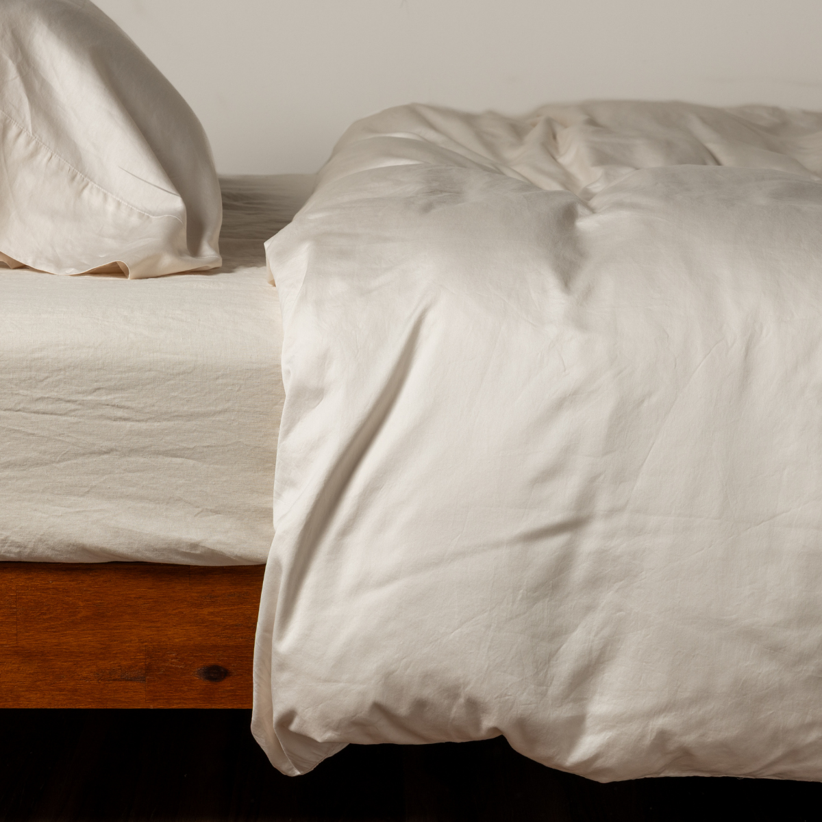Bella Notte Bria duvet cover in Natural, casually rumpled on a wood-framed bed.