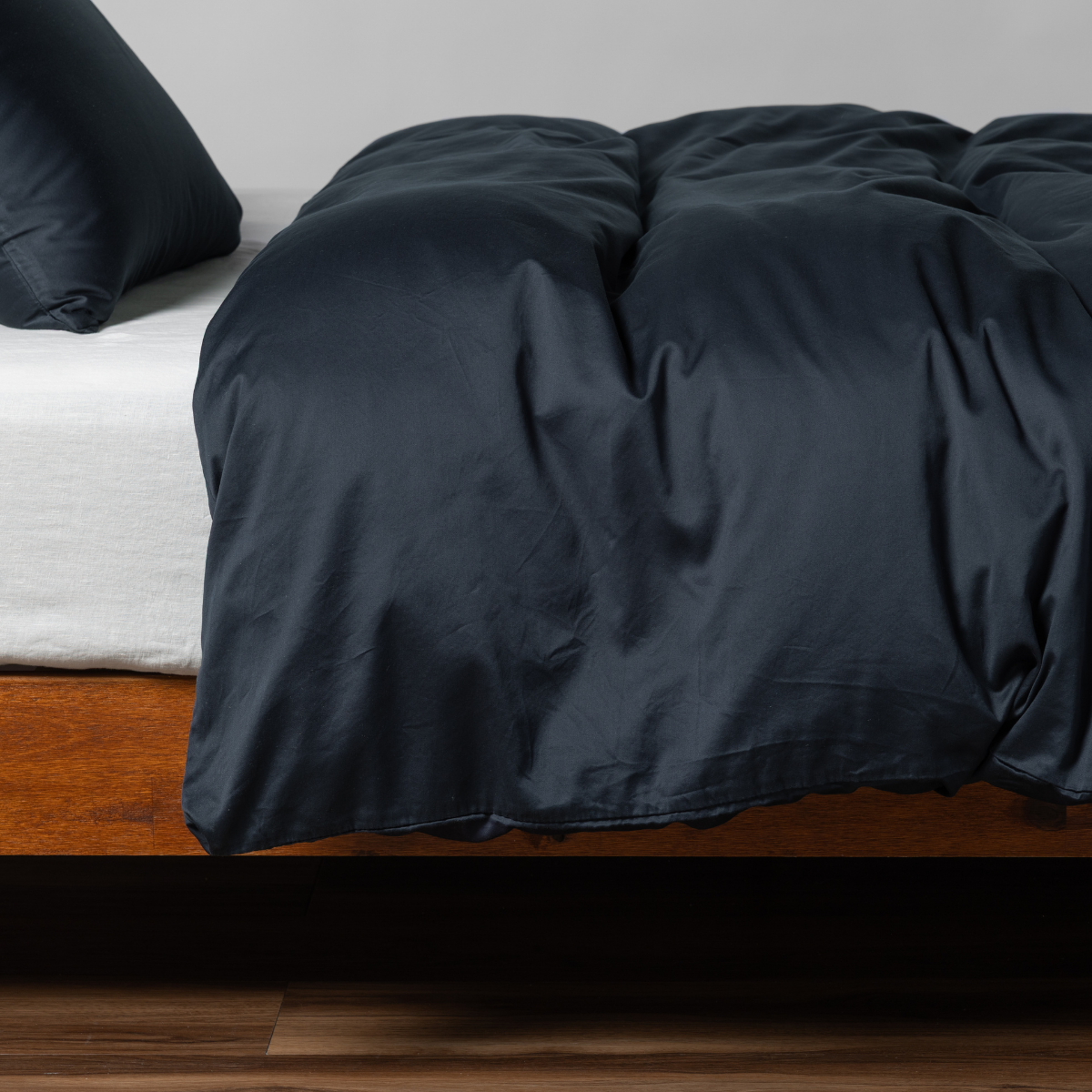 Angled view of Slate duvet cover draped over bed with walnut wood frame.