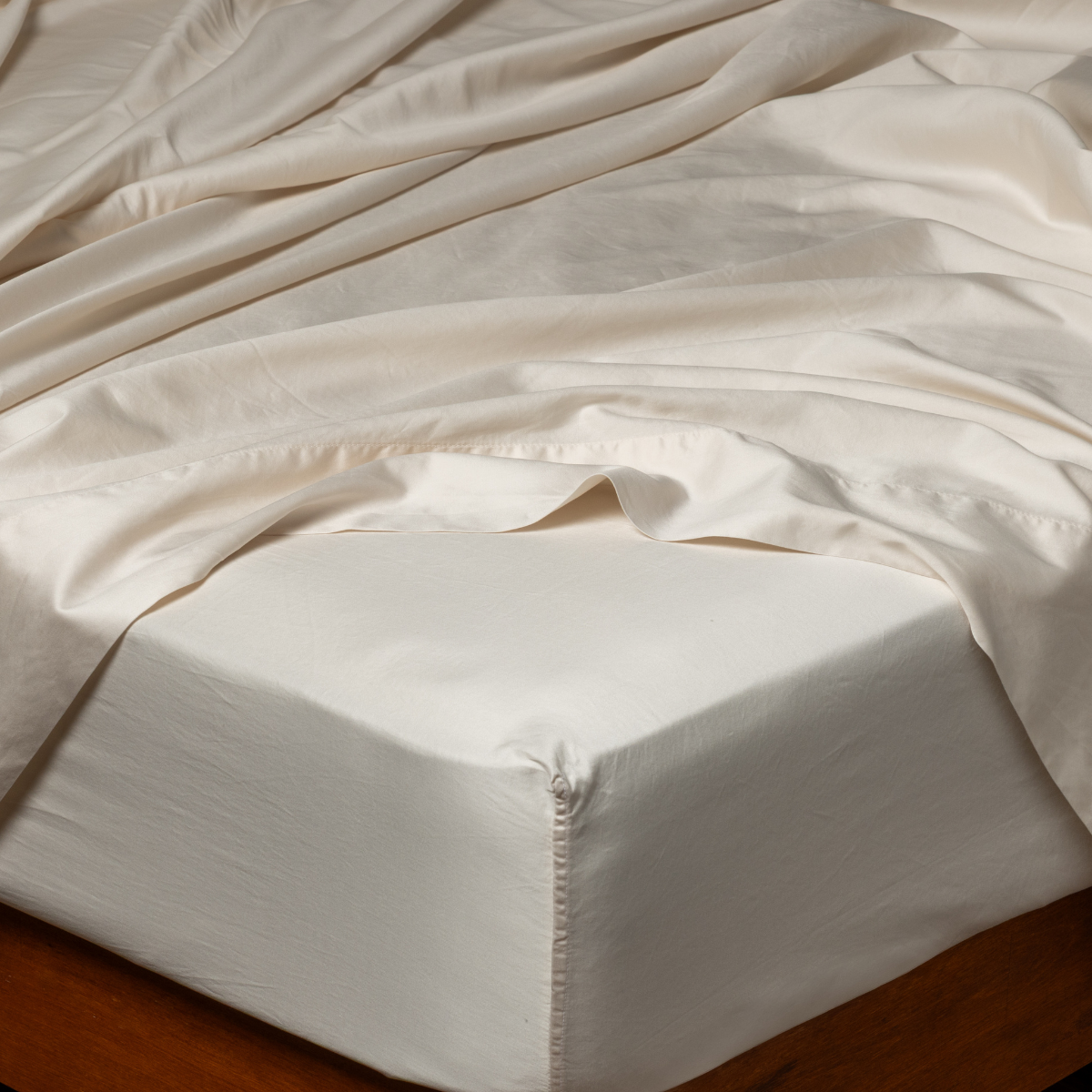 Bella Notte Bria fitted sheet in Natural, tucked corners on bed with softly draped fabric.