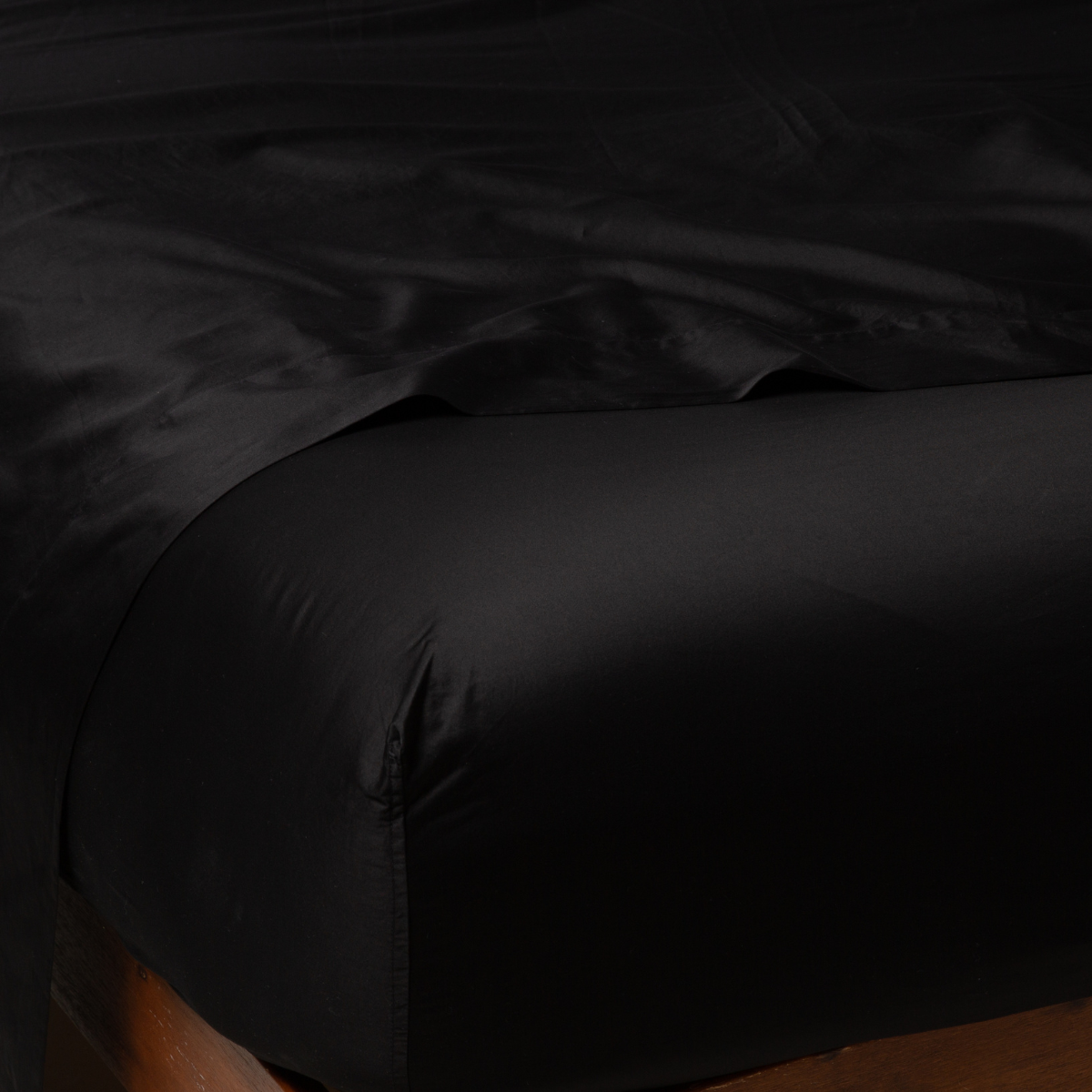 Corner view of Bella Notte Bria fitted sheet in Corvino, showing lustrous satin weave on wooden bed frame.