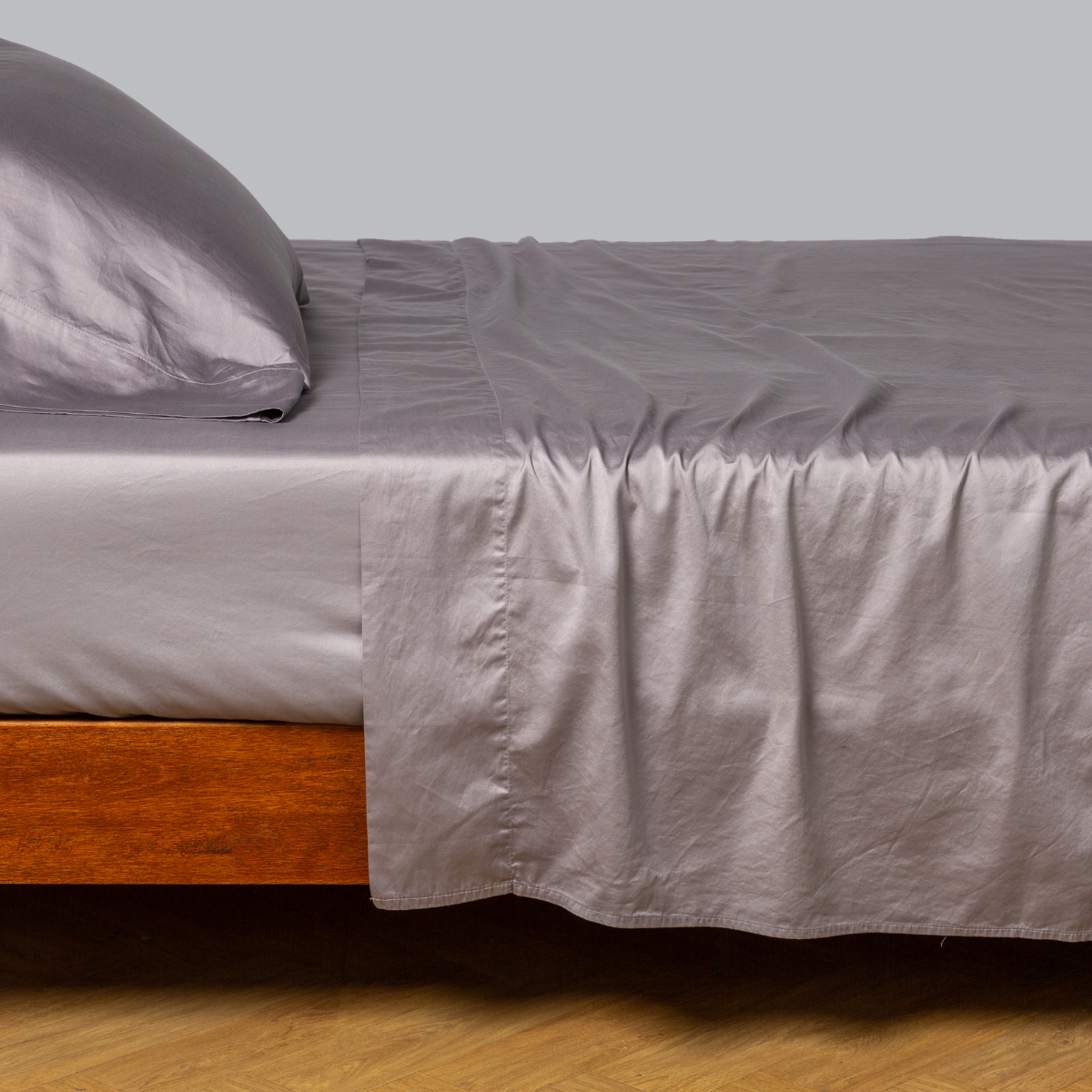 Bella Notte Bria fitted sheet in French Lavender, draped over a wood bed frame, side angle view.