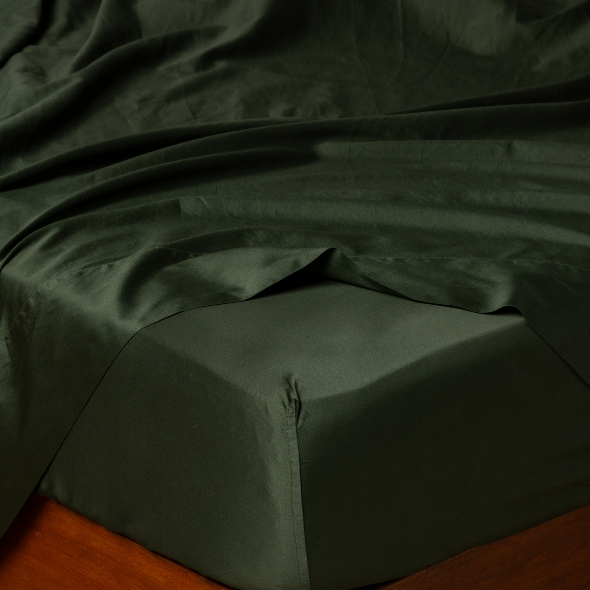 Close-up of Bria fitted sheet corner in Juniper, showing lustrous sateen drape on bed.