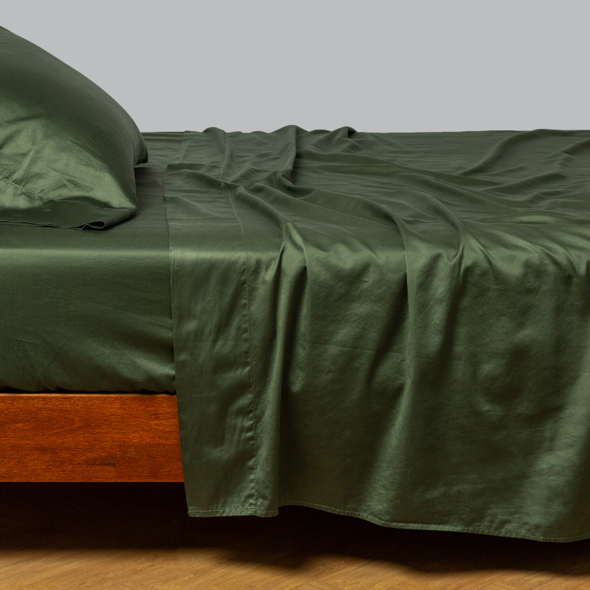 Juniper fitted sheet draped loosely over a wood-frame bed with matching pillowcases.