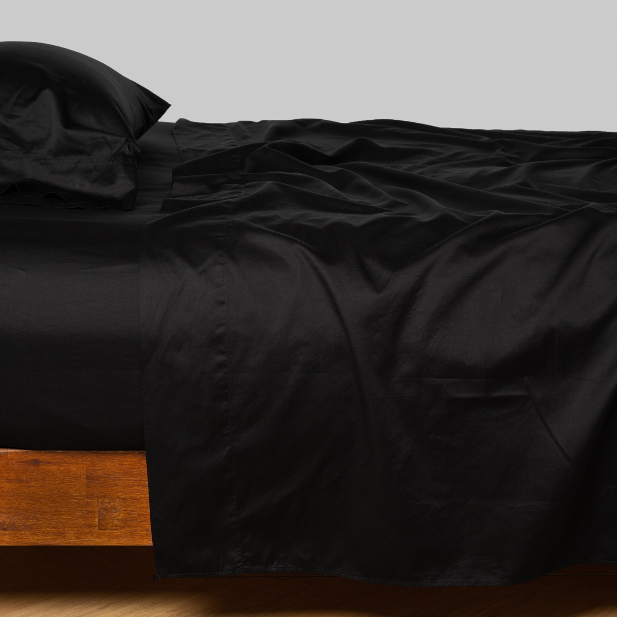 Corvino fitted sheet draped over wooden bed frame, deep black sateen finish with natural light sheen.