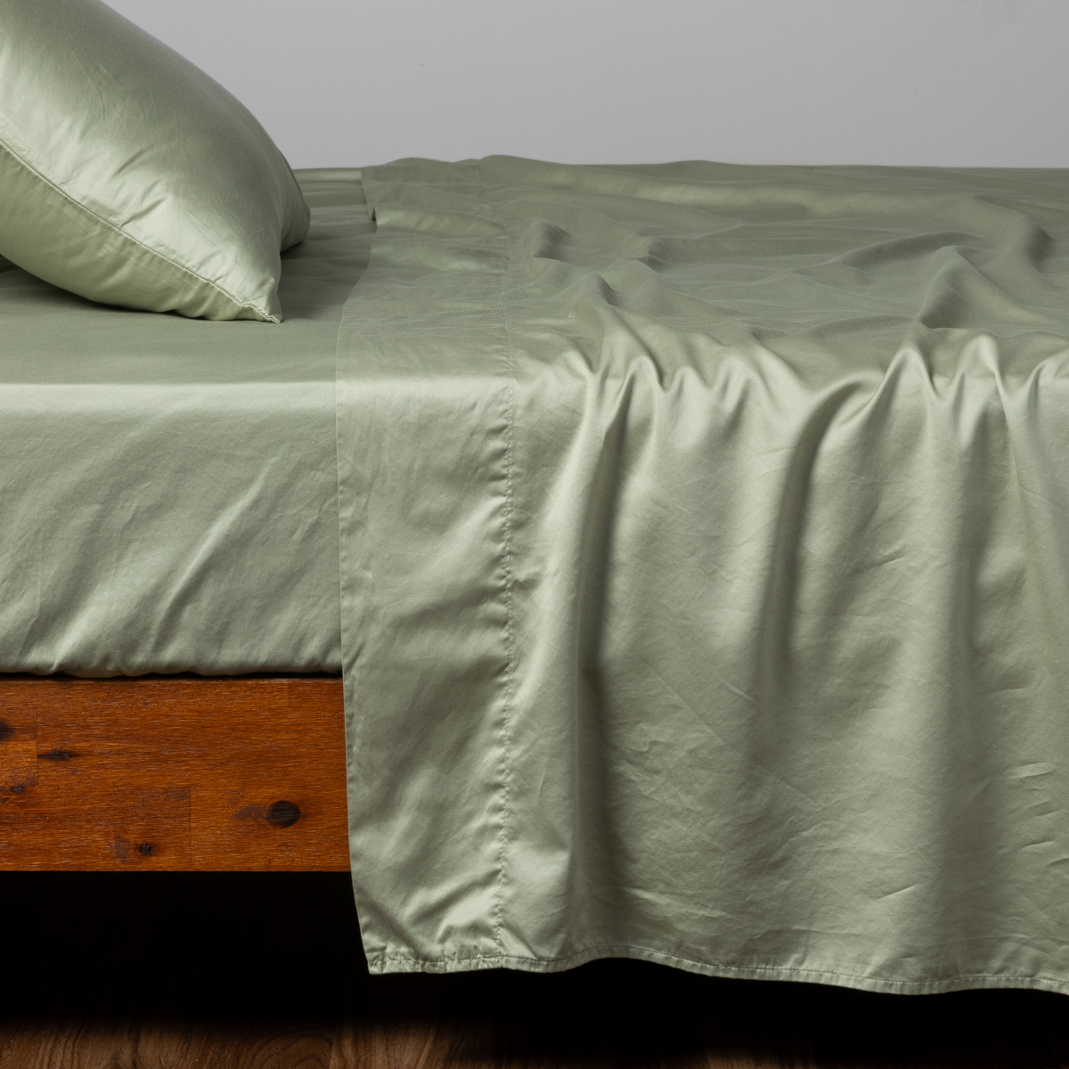 Desert Sage flat sheet draped over bed with matching pillowcase, silky sheen fabric.