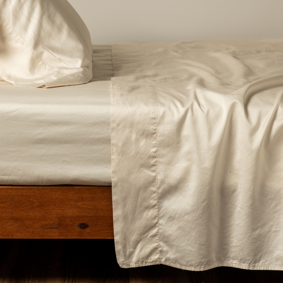 Bria fitted sheet in Natural draped over wood bed frame, ivory satin-finish fabric.